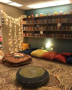 a room with many bookshelves and pillows on the floor in front of it