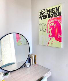 a mirror sitting on top of a wooden desk next to a wall mounted art piece