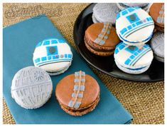 star wars themed cookies are sitting on a blue napkin next to a black plate with white frosting