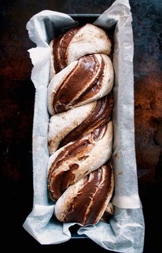 a loaf of bread wrapped in wax paper on top of a metal pan filled with chocolate frosting