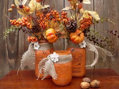 three mason jars filled with autumn flowers and fruit