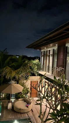 an outdoor deck with chairs and umbrellas next to a pool at night time,