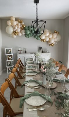 a dining room table set with place settings and balloons hanging from the ceiling above it