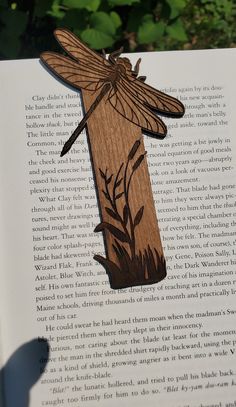 an open book with a wooden cut out of the shape of a dragonfly on it