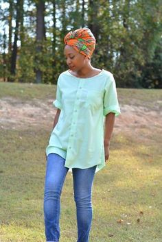 a woman standing in the grass wearing jeans and a green shirt with an orange head scarf