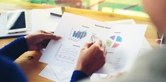 two people sitting at a table with papers and pens in front of them, looking at graphs