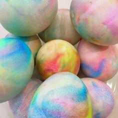 several dyed eggs in a glass bowl on a white tablecloth with blue, yellow and pink dye