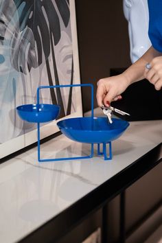 a person cutting into a blue bowl with scissors on a white counter top in front of a painting