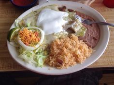 a white plate topped with lots of food next to a bowl of rice and beans