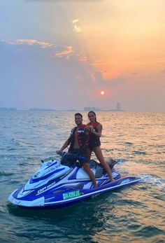 two people on a blue and white jet ski in the middle of the ocean at sunset