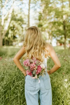 a woman standing in tall grass with her back to the camera holding a bouquet of flowers