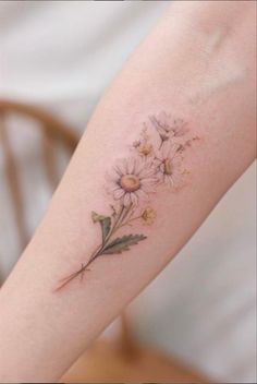 a woman's arm with daisies and leaves tattooed on the left side of her arm