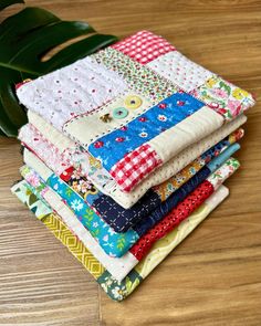 a stack of quilts sitting on top of a wooden table next to a green leaf