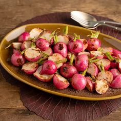 a yellow plate topped with radishes on top of a wooden table next to a fork