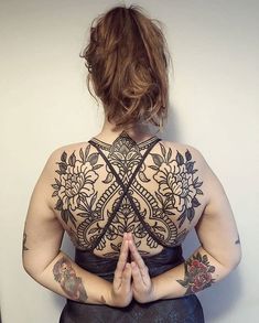 a woman with tattoos on her back standing in front of a wall and doing yoga