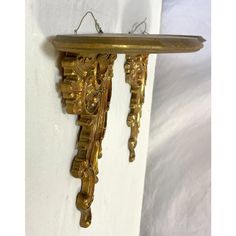 an ornate gold clock hanging from the side of a white wall next to a bed