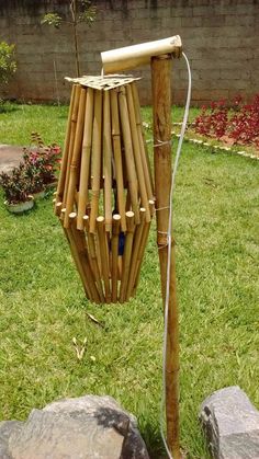 a bamboo wind chime in the middle of a yard with rocks and flowers behind it