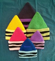 six crocheted hats are arranged on a blue surface, one is multicolored