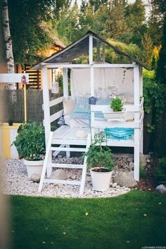 a white gazebo sitting in the middle of a lush green yard with potted plants