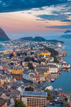 an aerial view of a city with water and mountains in the background at sunset or dawn