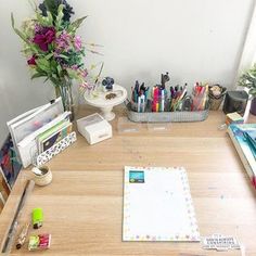 a wooden desk topped with lots of different types of pens and paper on top of it