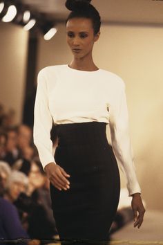 a woman is walking down the runway wearing a white top and black skirt with high heels