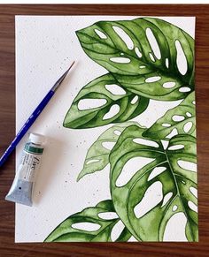 a watercolor painting of a green leaf on white paper next to a blue brush