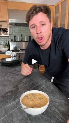 a man sitting at a table with a bowl of food in front of him and pointing to the camera