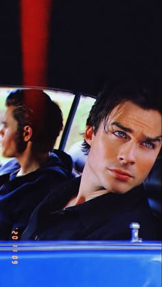 two young men sitting in the back seat of a car, one with blue eyes