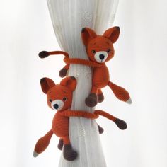 two knitted foxes hanging from the side of a curtain