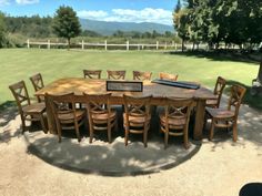 a large wooden table surrounded by chairs in the middle of a field with mountains in the background