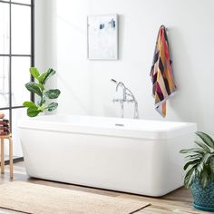 a white bath tub sitting on top of a wooden floor next to a potted plant