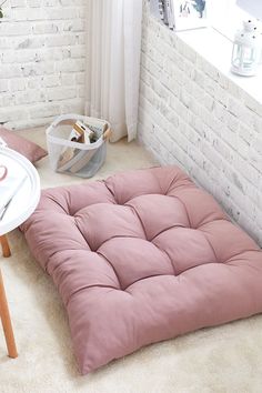 a futon mattress sitting on the floor in front of a white brick wall next to a table