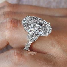 a close up of a person's hand holding an engagement ring with a pear shaped diamond