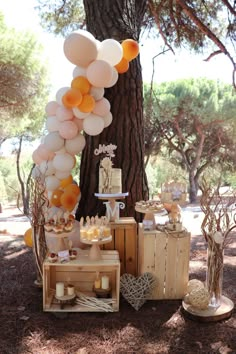 an outdoor dessert table with balloons, cake and other items on it in front of a tree