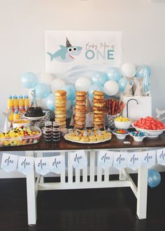 a table topped with lots of desserts and balloons next to a sign that says one