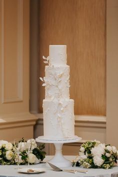 a white wedding cake sitting on top of a table next to flowers and silverware