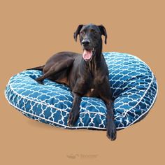 a black dog laying on top of a blue and white round bed with its tongue hanging out