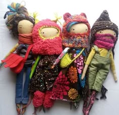 three dolls are laying next to each other on a white tablecloth covered surface with colorful crocheted clothing