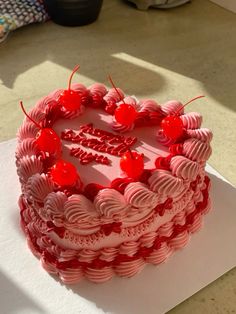 a red cake with white frosting and cherries sitting on top of a table