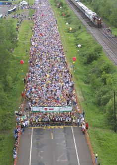 a large group of people standing on the side of a road next to train tracks