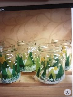 four glass jars with snow and flowers in them on a wooden table next to a wall