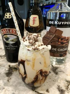 an ice cream sundae with chocolate and whipped cream in it next to bottles of booze