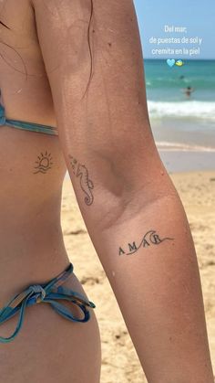 a woman with a tattoo on her arm standing in front of the ocean and beach