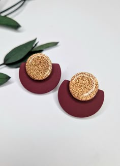 two pairs of gold and red earrings on top of a white table next to green leaves