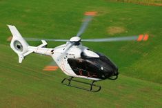 a white helicopter flying over a lush green field