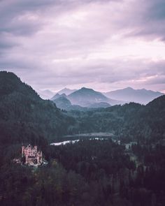 a castle sits on top of a hill surrounded by trees and mountains in the distance