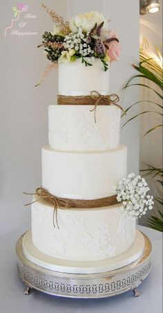 a three tiered white wedding cake with flowers on the top and ribbon around it