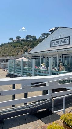 people are sitting at tables on the boardwalk by the beach in front of a restaurant