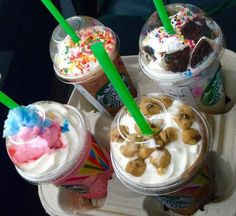 four different desserts in plastic cups on a tray with green straws and sprinkles